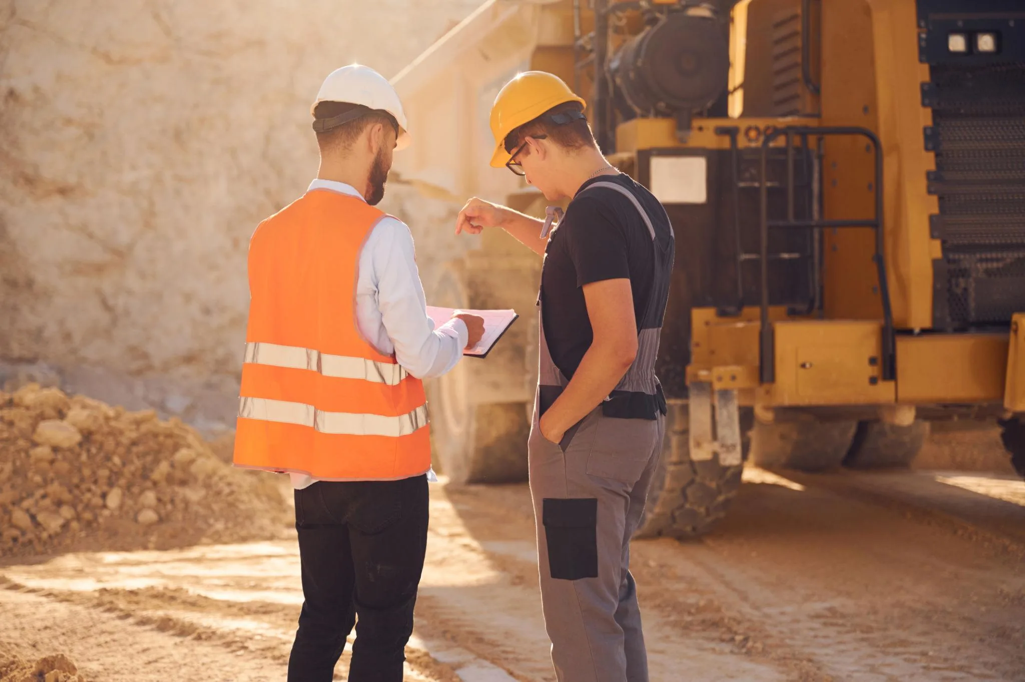 Two heavy-civil workers reviewing a field document beside haul equipment